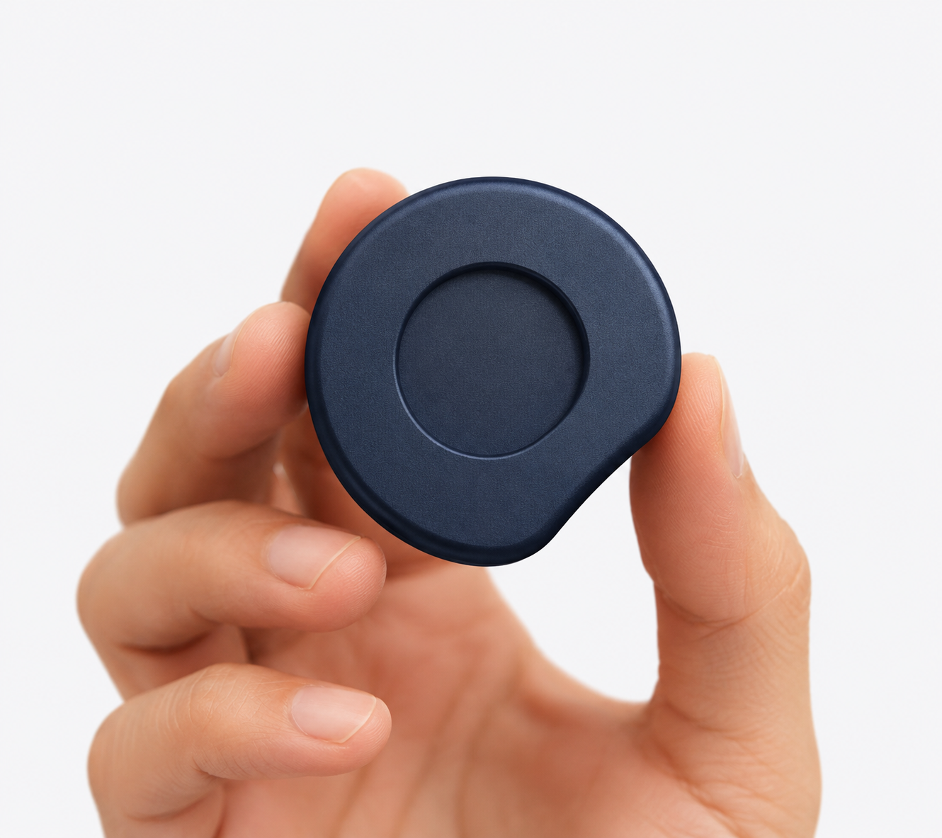 ORA held between two fingers, showing its compact size and textured navy finish